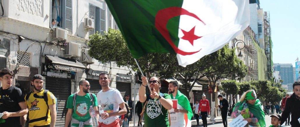 Des jeunes avec un drapeau de l'Algérie dans la rue.