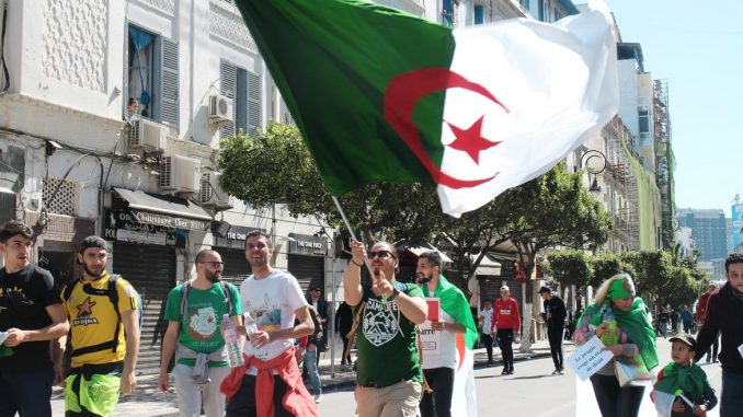 Des jeunes avec un drapeau de l'Algérie dans la rue.